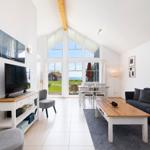 Living room with sofa, dining table, and large window overlooking the sea.