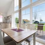 Dining area with table and chairs. Large windows offer view of terrace and beach.