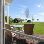 Terrace with table and chairs. View of green grass, houses, and sea.