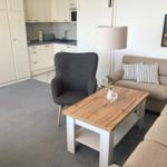 Living area with sofa, armchair, and table. Kitchen in the background.