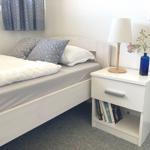 Bedroom with bed, nightstand, and lamp. Blue curtains and vase with flowers.