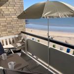 Balcony with umbrella, table, and chairs, view of beach and sea.