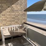 Terrace with table, chair, and umbrella. View of beach and sea.