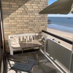 Terrace with table, chairs, and umbrella. View of beach and water.
