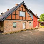Haus mit Backsteinfassade, rotem Anbau und Schieferdach. Außenbereich mit Grillplatz und Wohnwagen.