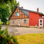Ein Haus mit roter Wand und Ziegelsteinfassade, umgeben von Grün und einem Kiesplatz.