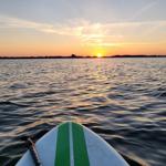 Sonnenuntergang auf dem Wasser mit Stand-Up-Paddleboard im Vordergrund.