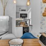 Küche mit Kühlschrank, Mikrowelle und Spülmaschine. Holztisch und blaue Stühle.