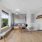 Wohnzimmer mit Sofa, Tisch und Sessel. Große Fenster und Holzboden.