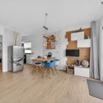 Wohnküche mit Esstisch, Kühlschrank und TV-Wand. Durchgang zur Schlafzimmer.