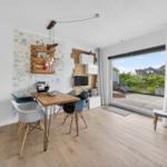 Essbereich mit Tisch und Stühlen, Wand mit Tapete und Holzregal, großes Fenster zur Terrasse.