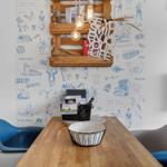 Esstisch mit blauen und grauen Stühlen vor blauem Tapetenwand mit Holzregal.