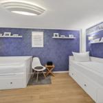 Zimmer mit zwei weißen Betten, blauer Wand und weißen Regalen.