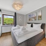 Schlafzimmer mit Doppelbett, Fenster mit Blick auf Grünfläche und Wandbildern mit Leuchtturm.