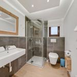Badezimmer mit Dusche, Waschbecken und Toilette. Holz- und Steinoptik.