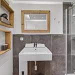 Badezimmer mit Dusche, Waschbecken und Holzregalen an der Wand.