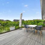 Terrasse mit Tisch, Stühlen und Sonnenschirm. Grünfläche und Blick auf Wohnhäuser.