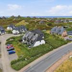 Haus mit Terrasse und Parkplatz, umgeben von Grünflächen und Blick aufs Meer.