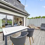 Terrasse mit Tisch, Stühlen und Liegen. Durchgehendes Glasfenster zum Innenraum.
