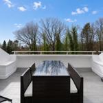 Terrace with table and chairs, view of trees and blue sky.