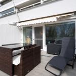Terrace with lounge furniture, table, and seating. Background: building with windows and white walls.