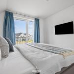 Schlafzimmer mit Blick auf Balkon und Strand. Bett, TV und blaue Vorhänge.