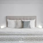Doppelbett mit Kopfkissen und Decke. Zwei Nachttische mit Lampen.