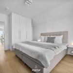Schlafzimmer mit Bett, Nachttisch und Kleiderschrank. Durchgang zum Wohnbereich mit Balkon.
