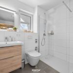 Badezimmer mit Dusche, Waschbecken und Toilette. Fenster mit Blick nach draußen.
