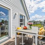 Terrasse mit Tisch, Stühlen und Blumen. Hintergrund: Wohnhäuser und Grünfläche.