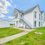 Moderne zweistöckige Villa mit Balkon und Außentreppe auf grünem Grundstück.