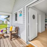 Haus mit Terrasse, Holzbank und Blick auf Grünflächen. Tür führt ins Innere.