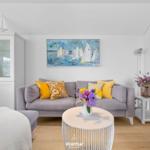 Ein Wohnzimmer mit grauem Sofa, gelben Kissen und einem runden Tisch.