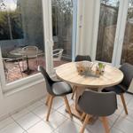 Runder Tisch mit vier Stühlen im Innenbereich, Blick auf Terrasse mit Tisch und Stühlen.