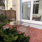 Terrasse mit Glas-Tisch und Stühlen, rote Pflastersteine und Holzzaun im Hintergrund.