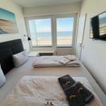 Schlafzimmer mit Blick aufs Meer, Bett mit Bettwäsche und TV.
