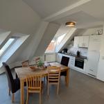 Essbereich mit Tisch und Stühlen unter Dachschrägen. Küche mit weißen Schränken und Fenster.