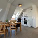 Essbereich mit Holztisch und Stühlen, angrenzende Küche mit weißen Schränken und Fenster.
