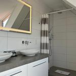 Badezimmer mit Dusche, Waschbecken und beleuchtetem Spiegel