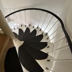 Spiralförmige Treppe mit schwarzem Teppich und weißem Geländer.
