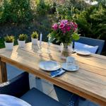 Holztisch mit Blumen, Tassen und Stühlen im Garten.