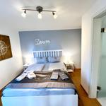 Schlafzimmer mit Bett, Nachttischen und Wanddekoration. Tür führt in Bad.