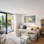 Wohnzimmer mit Sofa, Sessel, Glas-Tisch und Balkon. Wandbild und Bücherregal.
