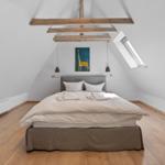 Schlafzimmer mit Dachschräge, Holzbalken, Bett und Fenster.