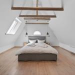 Schlafzimmer mit Dachschrägen, Holzboden und Bett unter Balken.