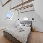 Schlafzimmer mit Dachschrägen, Holzboden und Dachfenster. Bett mit weißen Kissen und Bettwäsche.