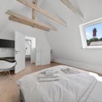 Schlafzimmer mit Blick auf Leuchtturm, Bett, Schreibtisch und Holzbalken.