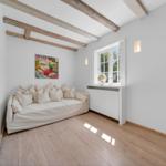 Raum mit Sofa, Fenster und Deckenbalken. Wandbild und Holzboden.