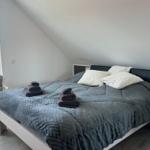 Schlafzimmer mit Dachschrägen, Bett mit grauer Bettwäsche und zwei Handtüchern.