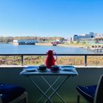 Balkon mit Tisch und Stühlen, Blick auf Wasser und Stadt.